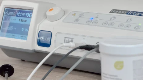 Medicinska naprava Human Tecar HCR 1002 za radiofrekvenčno terapijo, prikazana z aktivnim zaslonom in priklopljenimi elektrodami.