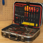 Profesionalni komplet orodja v kovčku, položen na delovni pult v delavnici, z izvijači, kleščami, ključavnicami in drugimi pripomočki za popravila.