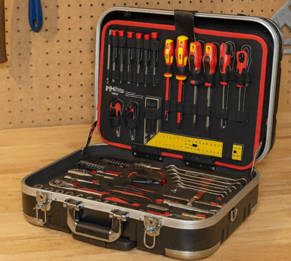 Profesionalni komplet orodja v kovčku, položen na delovni pult v delavnici, z izvijači, kleščami, ključavnicami in drugimi pripomočki za popravila.