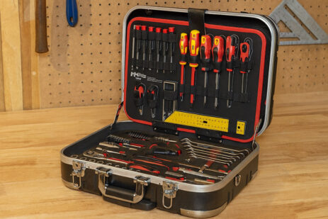 Profesionalni komplet orodja v kovčku, položen na delovni pult v delavnici, z izvijači, kleščami, ključavnicami in drugimi pripomočki za popravila.