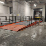 Industrijska notranja uporaba, kjer so nameščene oranžne nakladalne rampe z zaščitnimi ograjami, namenjene učinkovitemu pretovarjanju tovora v skladišču.