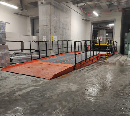 Industrijska notranja uporaba, kjer so nameščene oranžne nakladalne rampe z zaščitnimi ograjami, namenjene učinkovitemu pretovarjanju tovora v skladišču.